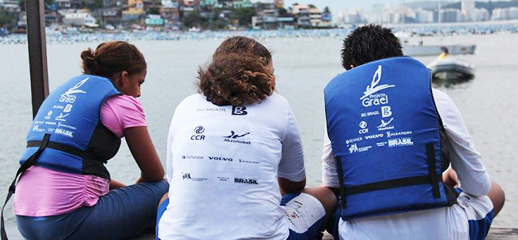 Imagem mostra três pessoas de costas olhando para o mar