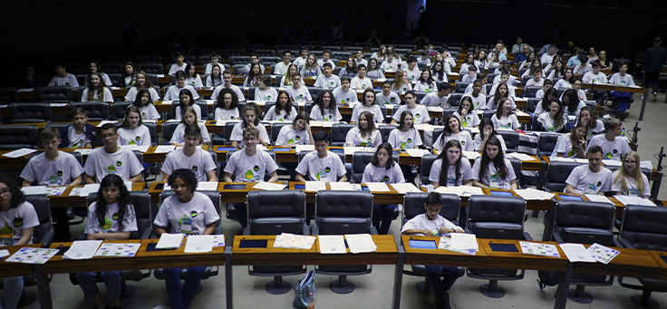 Imagem mostra grupo de crianças do projeto Câmara Mirim sentados em uma plenária
