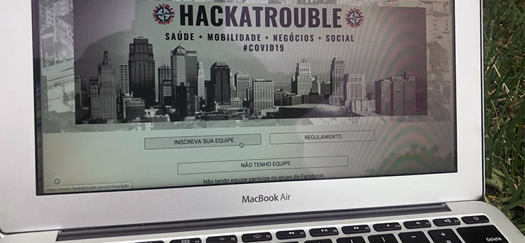 A imagem mostra o site do evento HackaTrouble, que uniu diversos profissionais em 48 horas de programação, em destaque na tela de um notebook.
