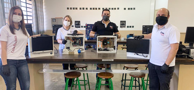 Quatro pessoas estão em sala de aula da ETEC de Pirsassununga ao lado de computadores feitos de peças de caça níqueis em projeto de tecnologia.