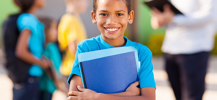 Imagem de uma criança de camiseta azul sorrindo enquanto segura alguns papeis azuis em suas mãos