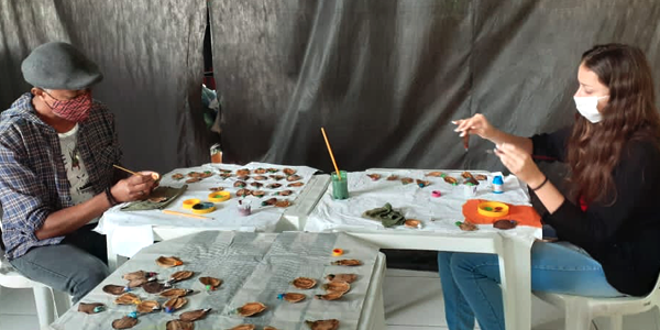 Dois jovens sentam de frente de um pro outro durante oficina de confecção de artesanato na Chácara das Flores durante a Semana dos Voluntários.