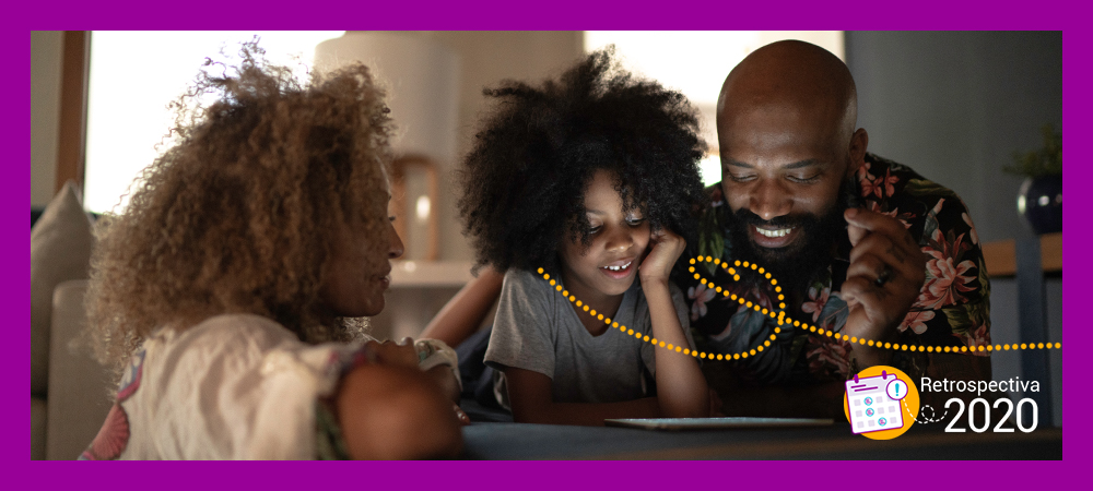 Imagem mostra uma família negra olhando para a tela de um tablet que está apoiado no sofá e sorrindo
