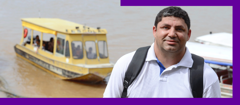 O Prof. Gilson da Silva, que atuou em escola atendida dentro do projeto Aula Digital, está sorrindo e, ao fundo, barcos se movimentam por rio que corta a cidade de Manaus (AM).