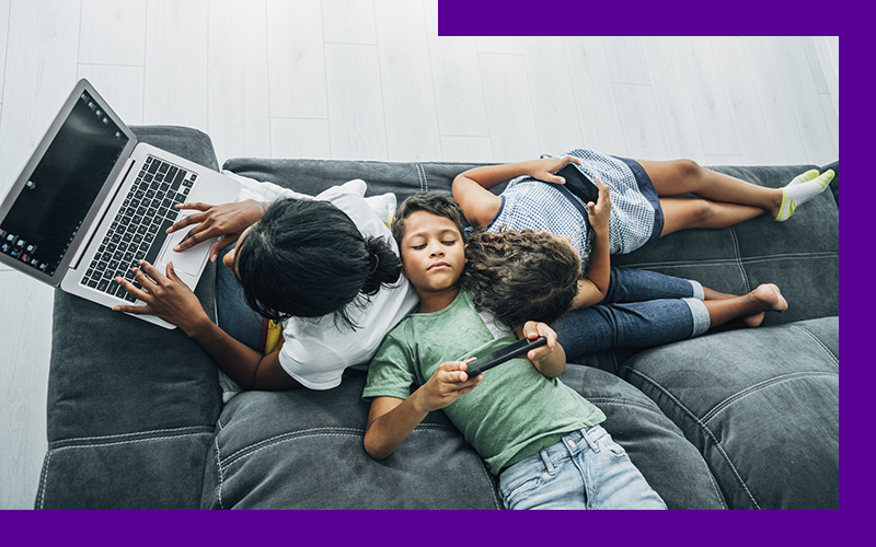 Imagem que ilustra o efeito do excesso de telas para crianças e adolescentes mostra três crianças apoiadas umas nas outras em um sofá. Uma delas usa um notebook , enquanto as outas duas estão olhando para as telas de smartphones.