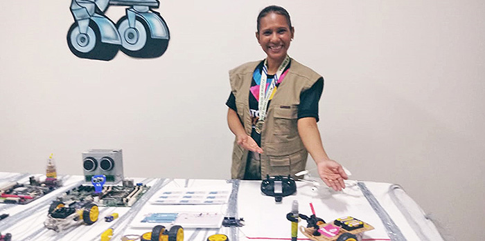 Professora Keila posa para foto atrás de uma mesa com diversos materiais utilizados em sua aula de robótica sustentável