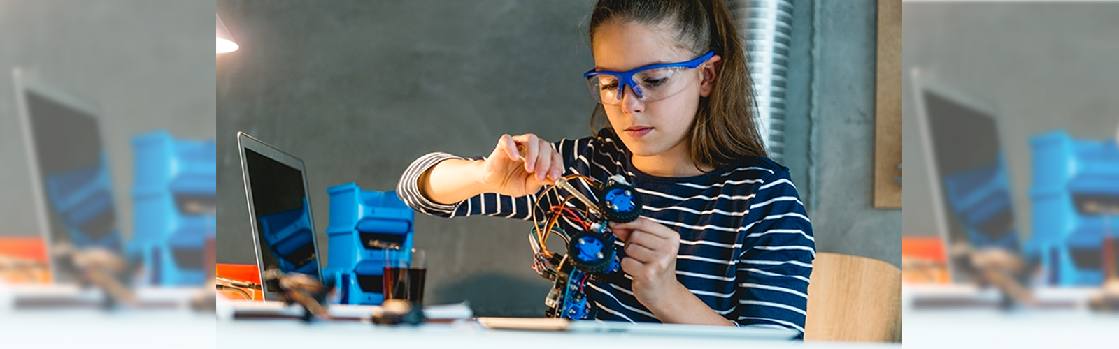 Menina está montando robô em uma bancada para representar pauta sobre a Coleção de Tecnologias Digitais. Ela usa óculos de proteção e tem os cabelos presos em rabo de cavalo.
