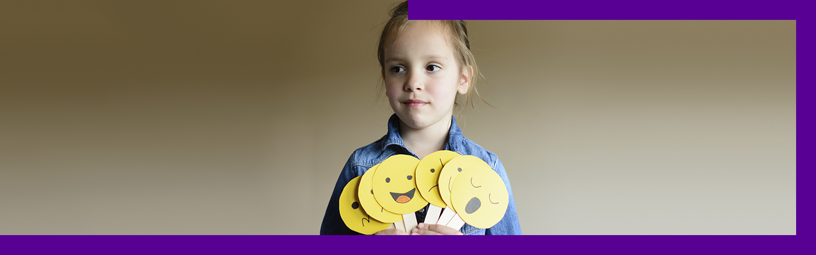 Em imagem que ilustra como ajudar as crianças a se expressarem, uma menina segura diversas placas que lembram emojis de expressões faciais, indicando sono, alegria, tristeza, entre outros. Ela está olhando para a frente com um sorriso discreto.