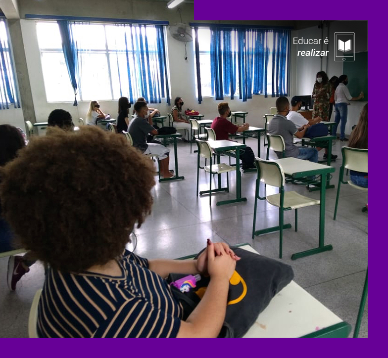 A pauta Educar é realizar traz a imagem de uma sala de aula em que um grupo de aproximadamente dez pessoas estão sentadas em carteiras olhando para três educadoras que estão afrente da sala, próximas à lousa.