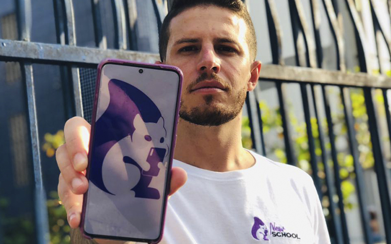 Plataforma New School une voluntariado e educação para ajudar jovens da periferia. Na imagem, Jotapê, o fundador da iniciativa está segurando um celular que mostra uma das telas do aplicativo.