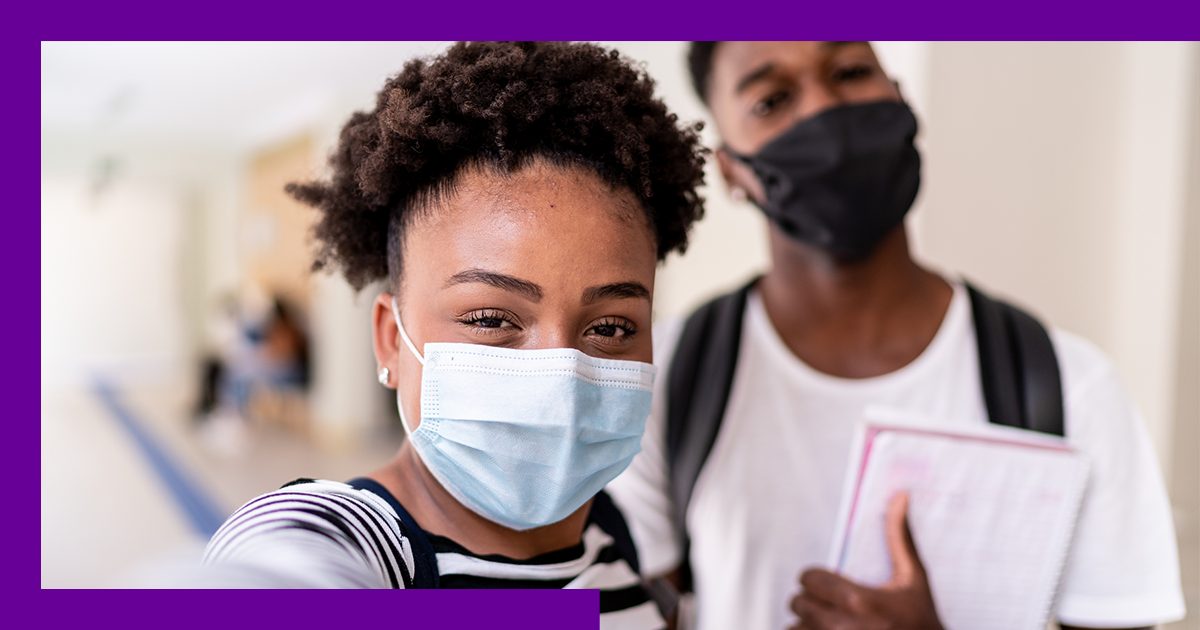 Imagem mostra em destaque dois estudantes jovens no corredor da escola, usando máscara de proteção individual
