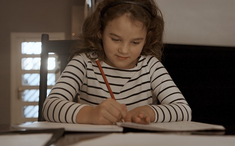 Imagem de uma menina escrevendo em folhas de papel.