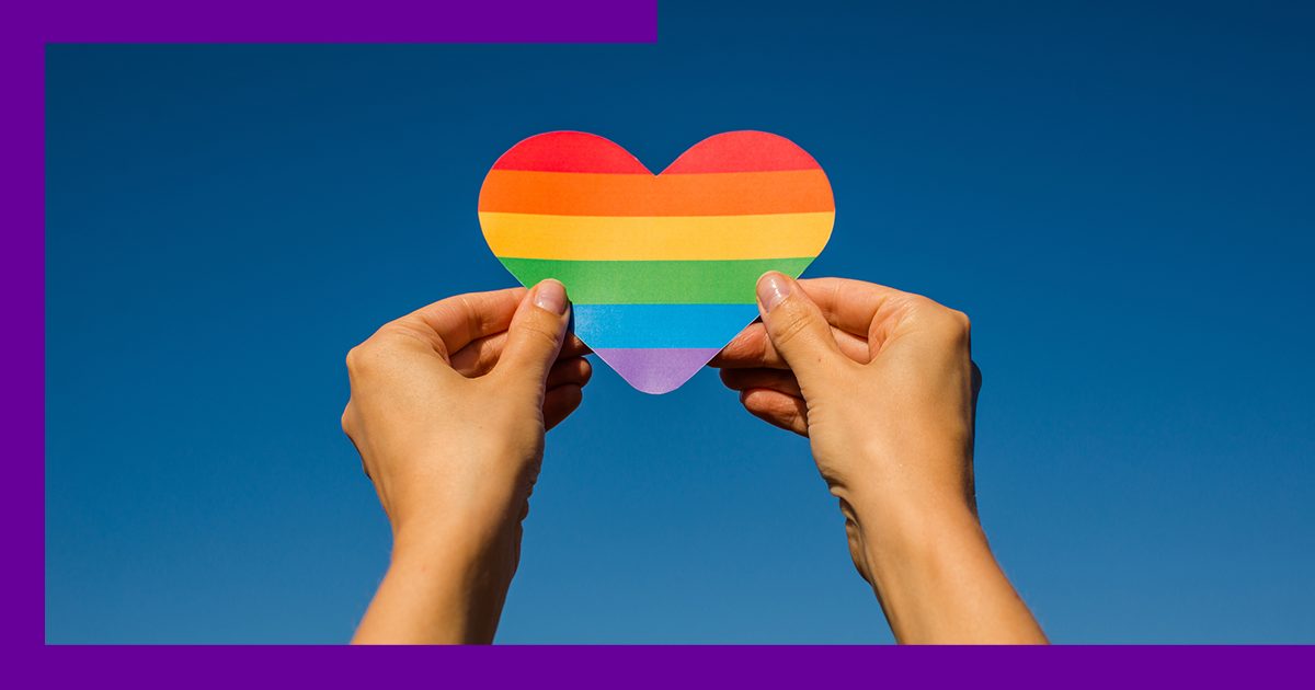 Imagem de uma pessoa levantando um coração de papel com as cores de um arco-íris.