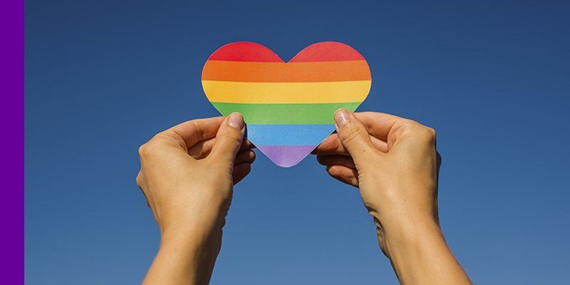 Imagem de uma pessoa levantando um coração de papel com as cores de um arco-íris.