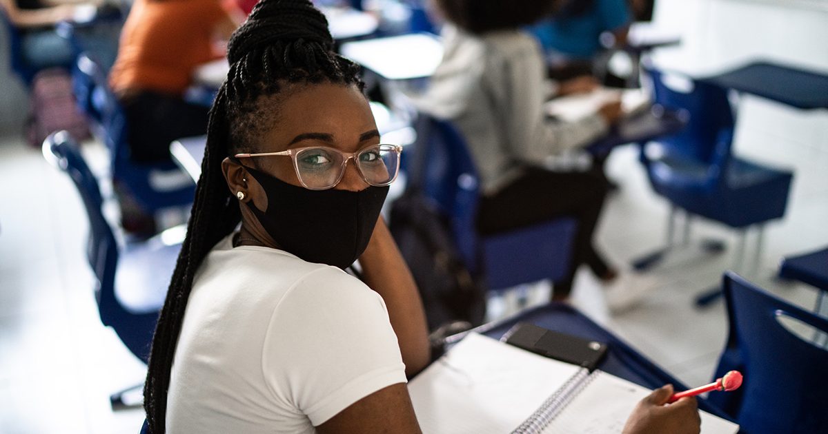 Imagem de uma estudante em sala de aula usando máscara