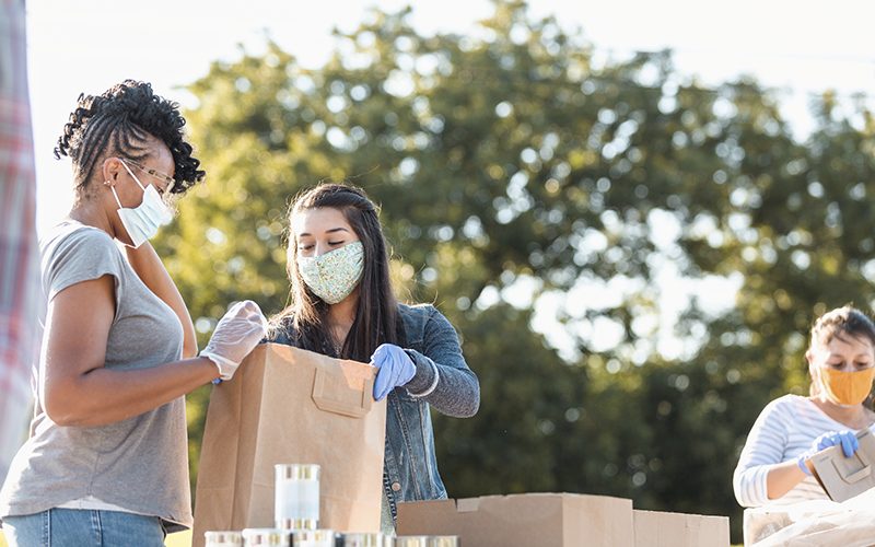 Imagem de três pessoas, voluntárias, distribuindo mantimentos