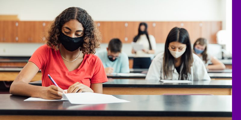 Imagem de estudantes fazendo prova em sala, com máscaras e distanciamento social