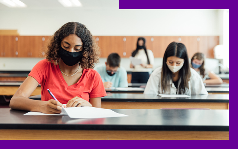 Imagem de estudantes fazendo prova em sala, com máscaras e distanciamento social