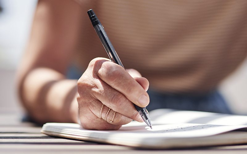 Imagem de parte de uma mulher escrevendo em um caderno