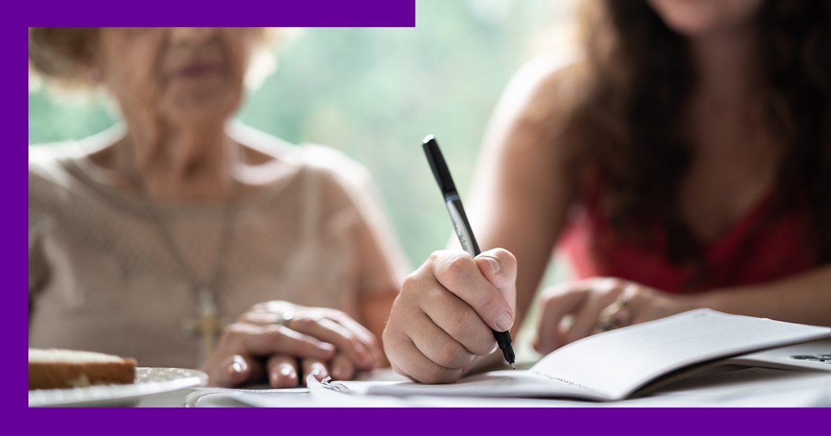 imagem de duas mulheres lado a lado, uma senhora e uma jovem, com destaque para as mãoes da jovem escrevendo em um caderno.