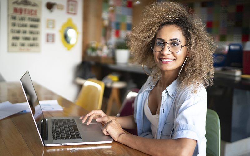 imagem de uma mulher sorrindo em uma sala residencial sentada em frente a um computador