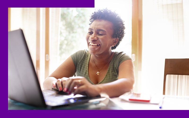 Imagem mostra professora negra sorrindo e digitando em um notebook