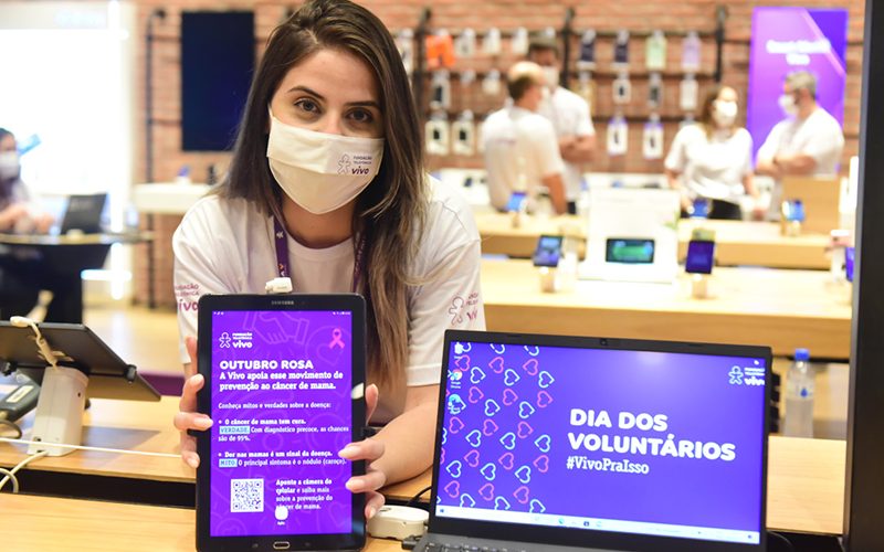 Imagem mostra voluntária em uma loja Vivo segurando um tablete com informações sobre a campanha outubro rosa e prevenção ao câncer de mama
