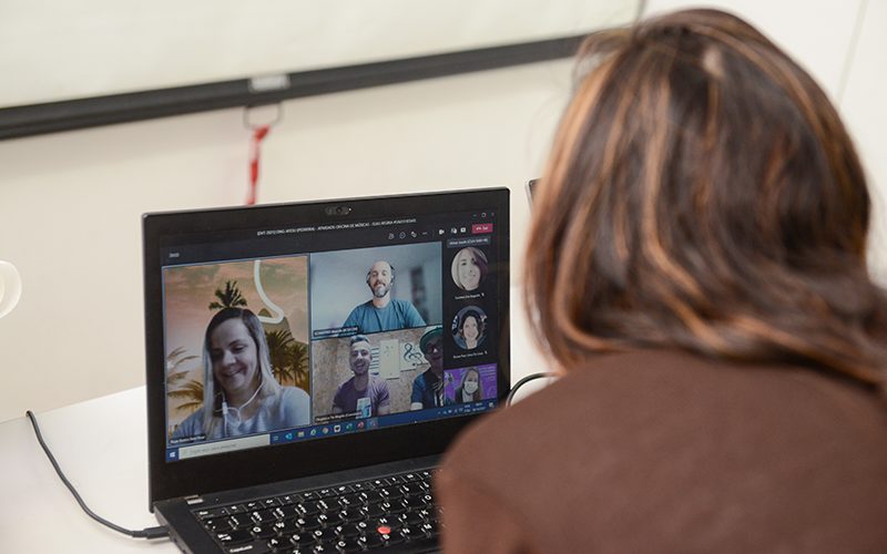 Imagem mostra voluntária usando o computador. Ela está assistindo a uma live com participantes em sua tela.