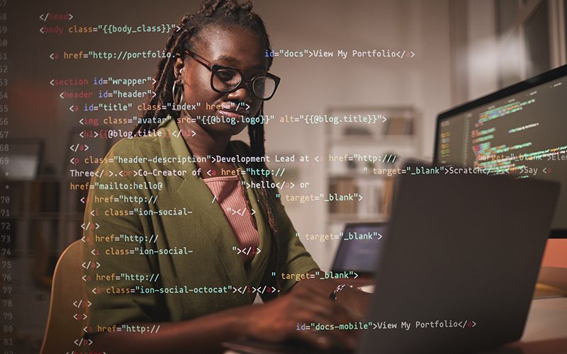 Imagem mostra uma jovem negra, ela usa óculos e tem cabelos compridos. Ela está usando um computador. Sobre toda a imagem, há códigos que costumam ser usados em linguagem de programação