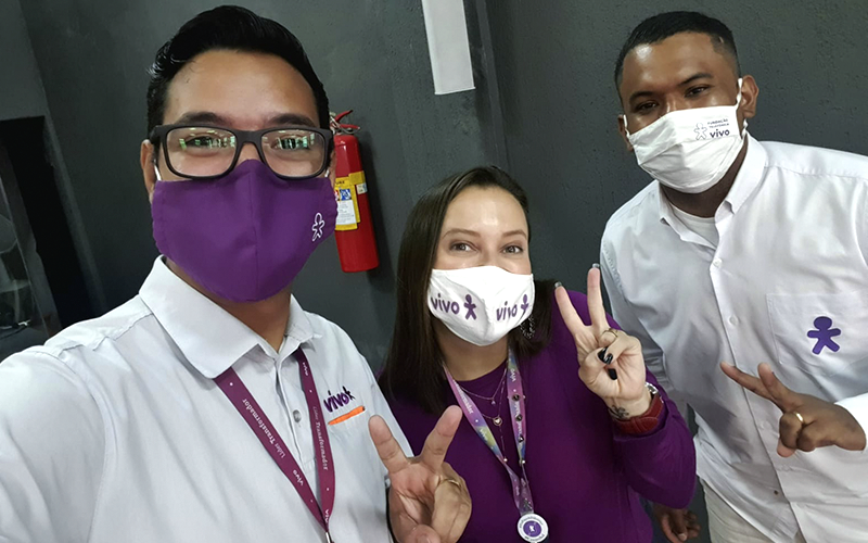 Imagem mostra três voluntários, sendo dois homens e uma mulher. Eles usam máscara e sorriem para a foto.