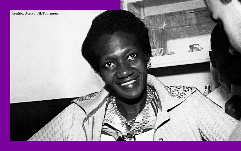 Imagem mostra a escritora Carolina Maria de Jesus sorrindo para a foto. Ela é negra, usa um casaco em cor clara, uma camisa também em cor clara e alguns colares.