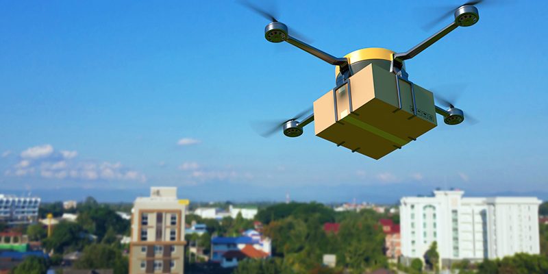 Imagem mostra um drone sobrevoando uma cidade. É possível ver habitações como prédios e casas ao fundo na imagem.
