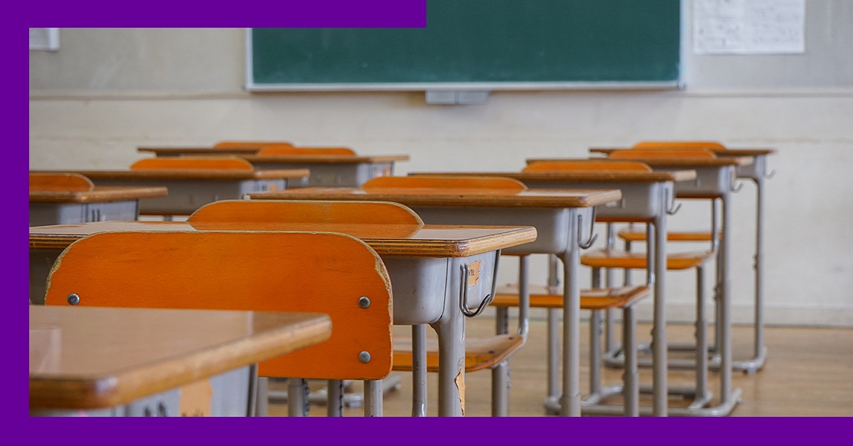 Imagem mostra uma sala de aula com uma série de cadeiras vazias. É possível ver uma lousa no fundo da imagem