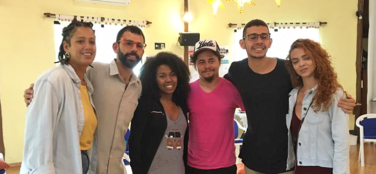 Cinco jovens que participam da Imersão do Pense Grande estão posando lado a lado da empreendedora Ana Carolina Martins, que usa blusa amarela embaixo de camisa azul claro e foi a empreendedora referência da atividade do Aquário.