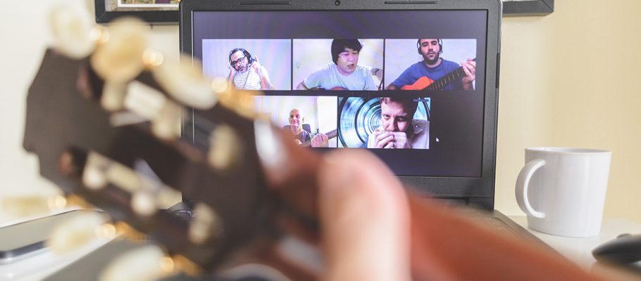 Imagem mostra artistas que se reinventaram na pandemia. Um braço de violão aparece desfocado em frente a uma tela de notebook aberta em uma chamada de vídeo com várias pessoas.