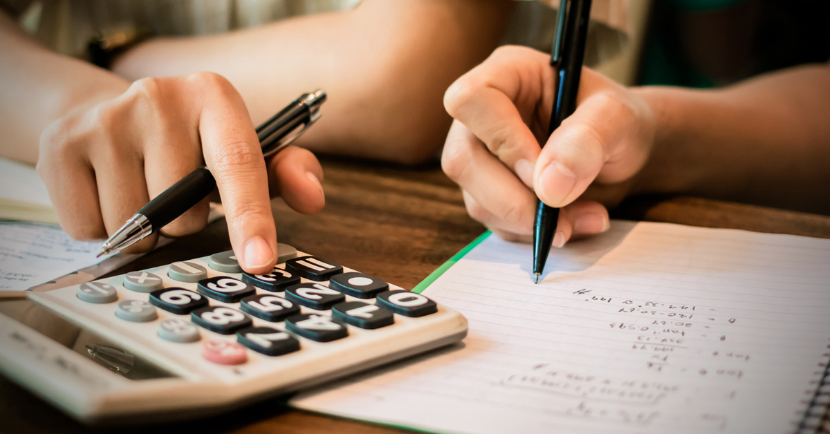 Imagem da pauta sobre educação financeira mostra em detalhes as mãos de duas pessoas, uma delas digita na calculadora, enquanto a outra anota números em um caderno