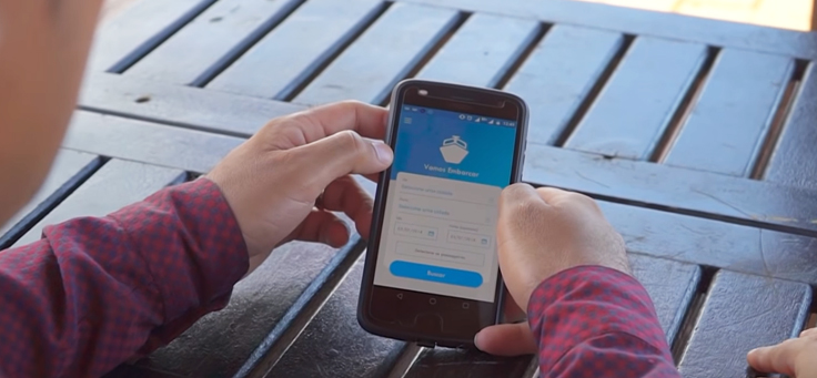 A imagem mostra o detalhe de duas mãos segurando um celular onde na tela se vê a interface no aplicativo Embarcar