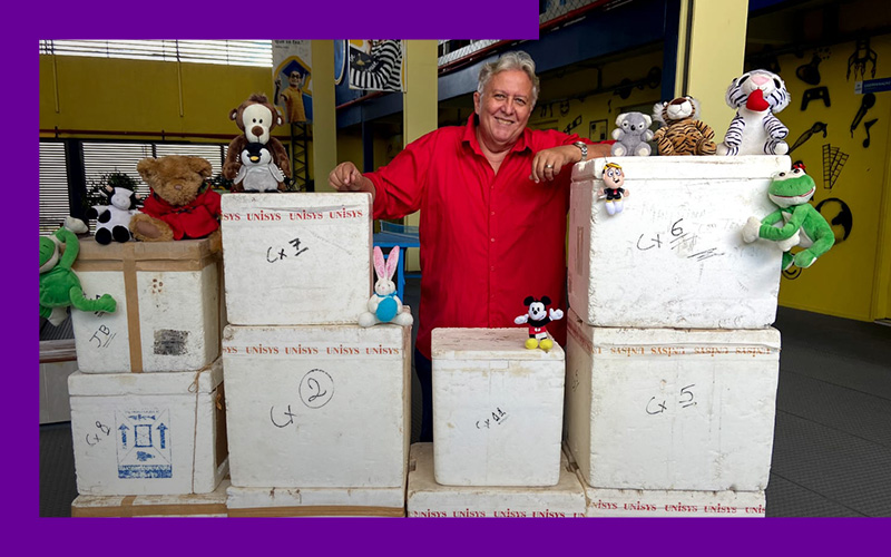 O professor Antero Macedo posa com as caixas de isopor repletas de cartas que seus ex-alunos escreveram na adolescência. Ele é um senhor branco, de cabelos grisalhos e veste uma camisa vermelha de botões.