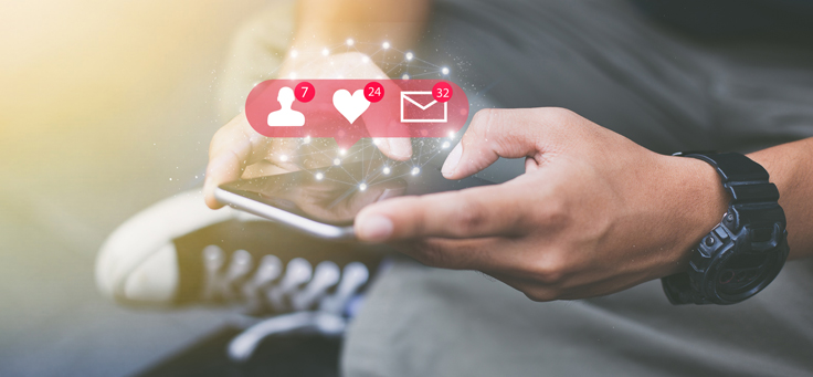 Imagem que representa pauta sobre influenciadores digitais mostra uma pessoa jovem de pernas cruzadas utilizando um smartphone. No centro da imagem há uma arte que remete a ícones de redes sociais que representam novas mensagens, favoritos e novo contato.