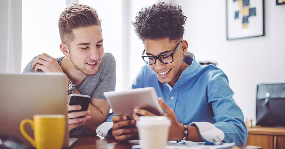 Dois jovens estão sentados lado a lado olhando para telas de dispositivos móveis para representar live sobre tecnologia e empreendedorismo social.