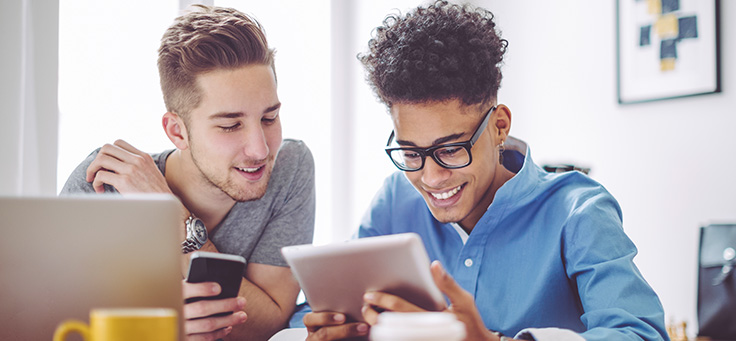 Dois jovens estão sentados lado a lado olhando para telas de dispositivos móveis para representar live sobre tecnologia e empreendedorismo social.
