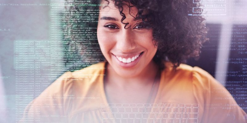 Imagem mostra uma jovem negra sorrindo. Por cima de sua imagem, é possível ver códigos de programação e o teclado de um computador. A jovem usa uma camisa na cor laranja.