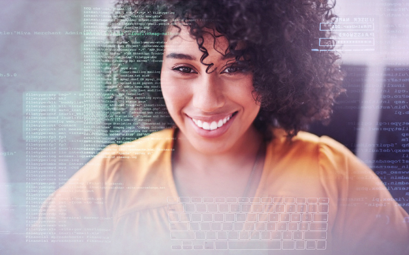 Imagem mostra uma jovem negra sorrindo. Por cima de sua imagem, é possível ver códigos de programação e o teclado de um computador. A jovem usa uma camisa na cor laranja.