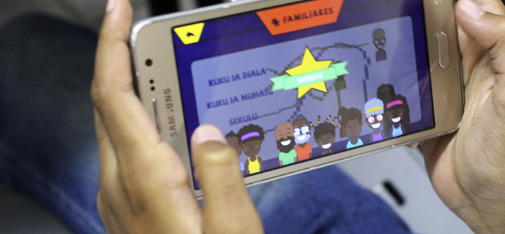 Imagem mostra mão de criança segurando um smartphone cuja tela mostra o aplicativo Alfabantu, que ensina o idioma kimbundu, de Angola