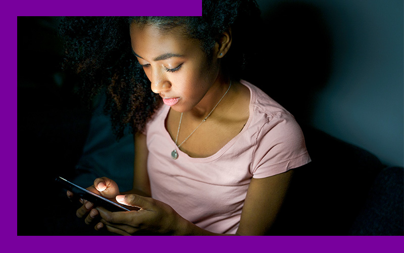 Imagem mostra uma menina negra utilizando um celular.