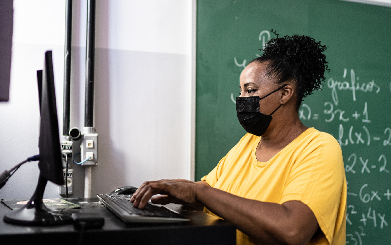 Foto de professora sentada, usando um computador, reforçando o posicionamento da Fundação Telefônica Vivo de Educar para Digitalizar