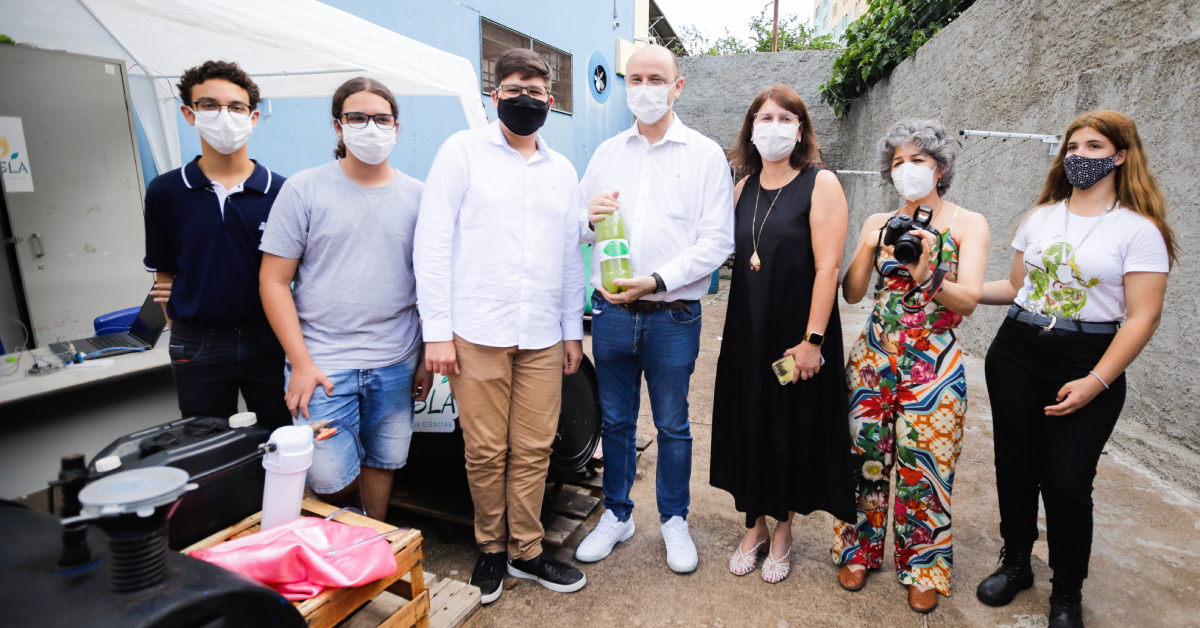 Alunos e professores posam para foto com biogás em uma garrafa pet, resultado do projeto de ciências Tesla.