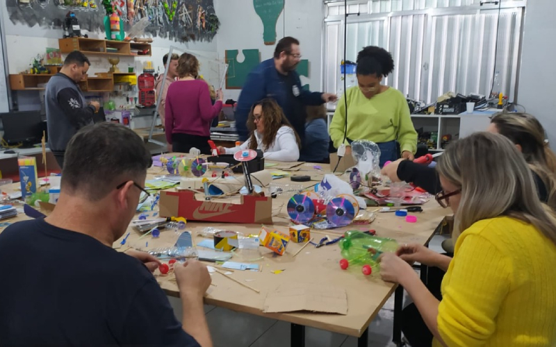 Professores reunidos em torno de uma mesa com sucatas diversas para a construção de protótipos eletrônicos em formação docente em robótica educacional