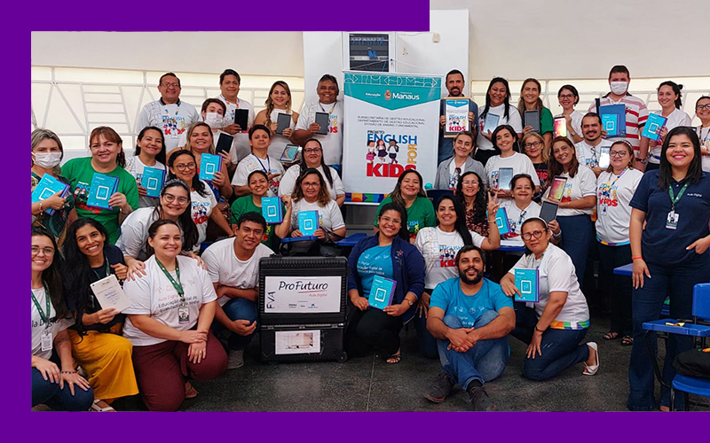 Imagem mostra grupo de educadores de Manaus reunidos em uma sala de aula. Entre eles, é possível ver a maleta do Aula Digital e um banner com o nome do projeto English for Kids