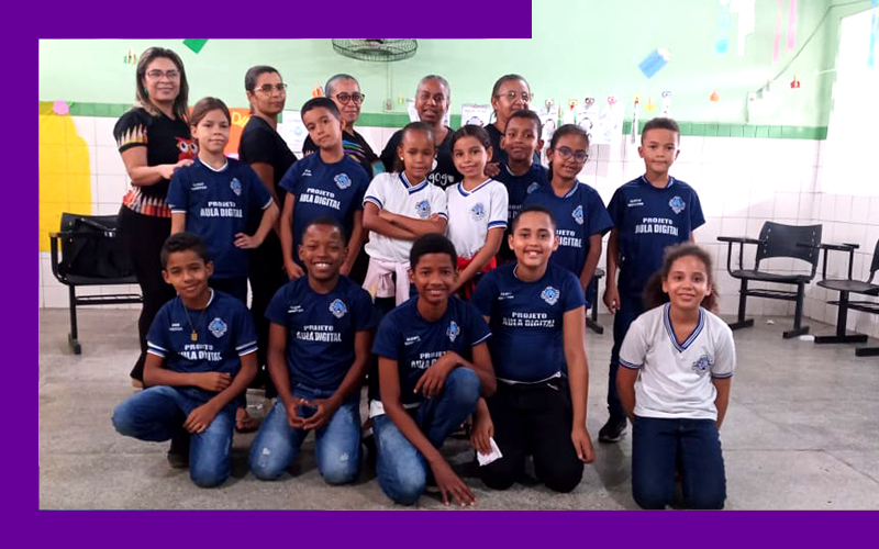 Na imagem, vemos um grupo de 12 crianças que são alunos monitores do Aula Digital no Sergipe, em uma sala de aula reunidos com cinco professoras